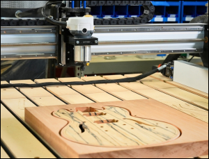 LongMill MK3 4 | Sienci Labs CNC router milling a wooden guitar body on a machine bed, shaping the blank into curves and cavities.