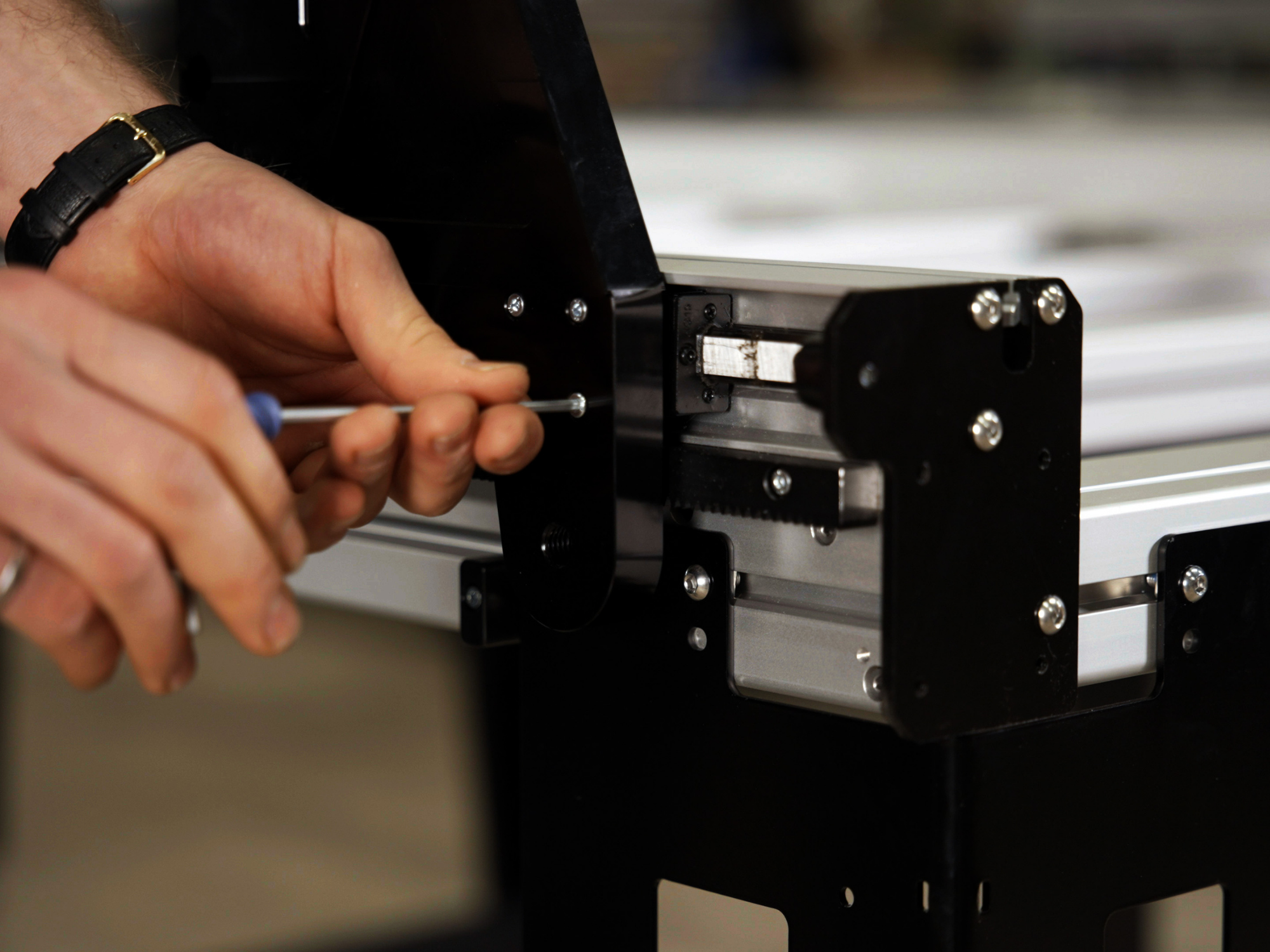 Close-up of a person’s hands tightening a screw on a black metal frame with silver rails and bolts