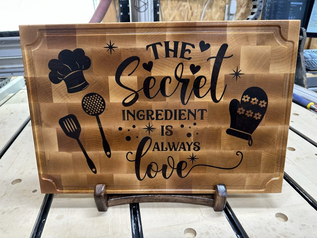 Decorative wooden sign that reads, 'The Sweet Secret Ingredient Is Love' with utensil silhouettes and hearts.